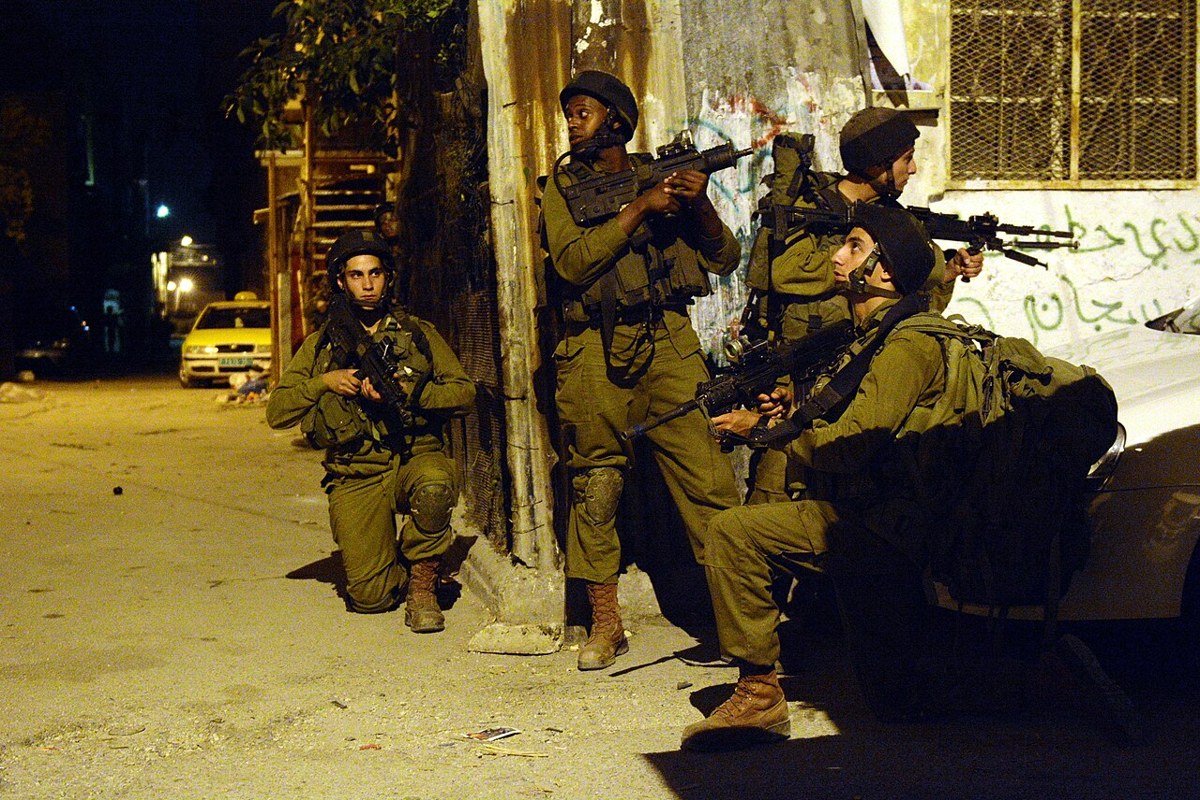 Israeli soldiers with rifles take positions on a street in the Hebron area at night